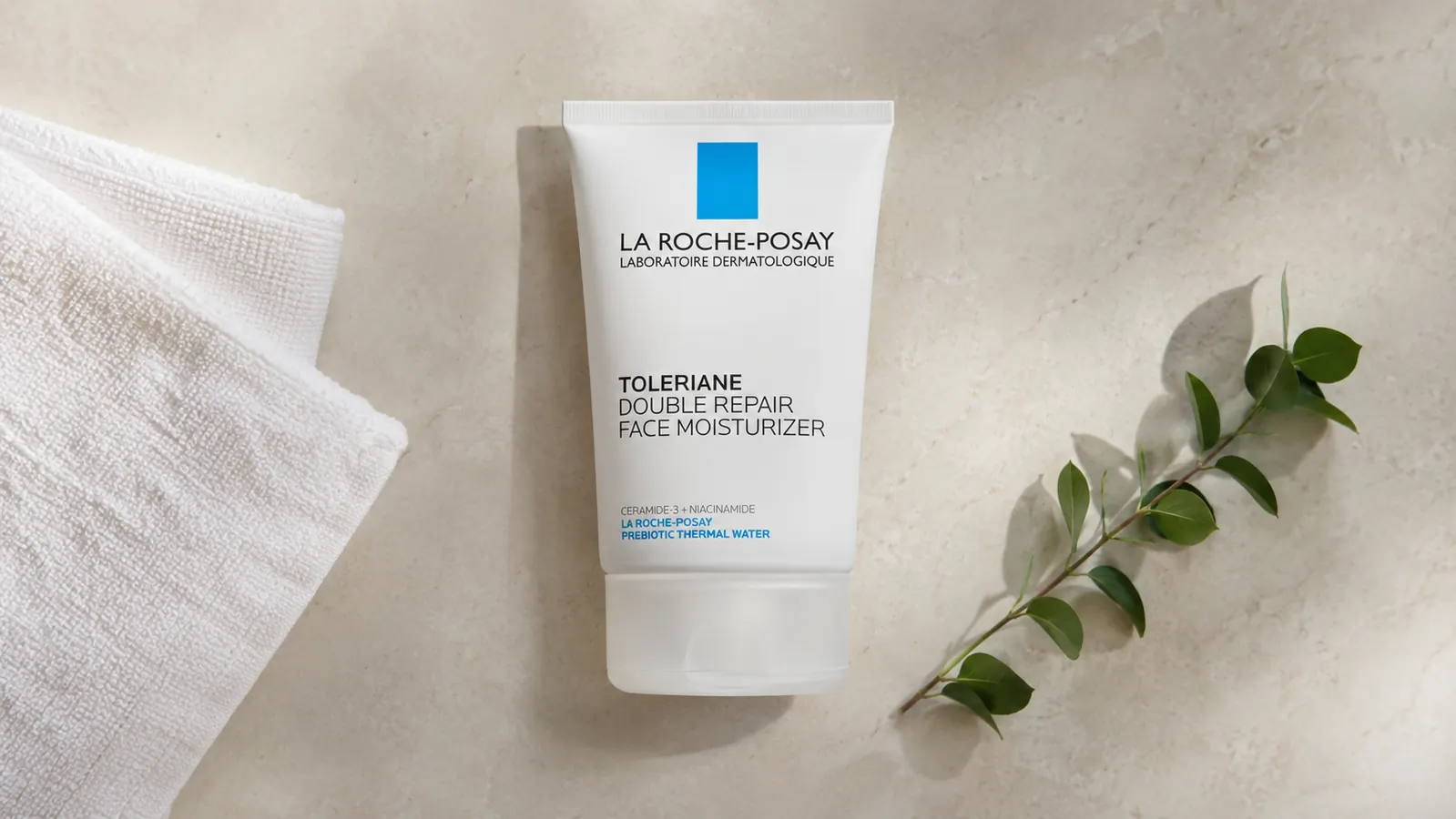 Skincare flat-lay showing the La Roche-Posay Toleriane moisturizer alongside a clean cotton towel and a small plant on a cream surface