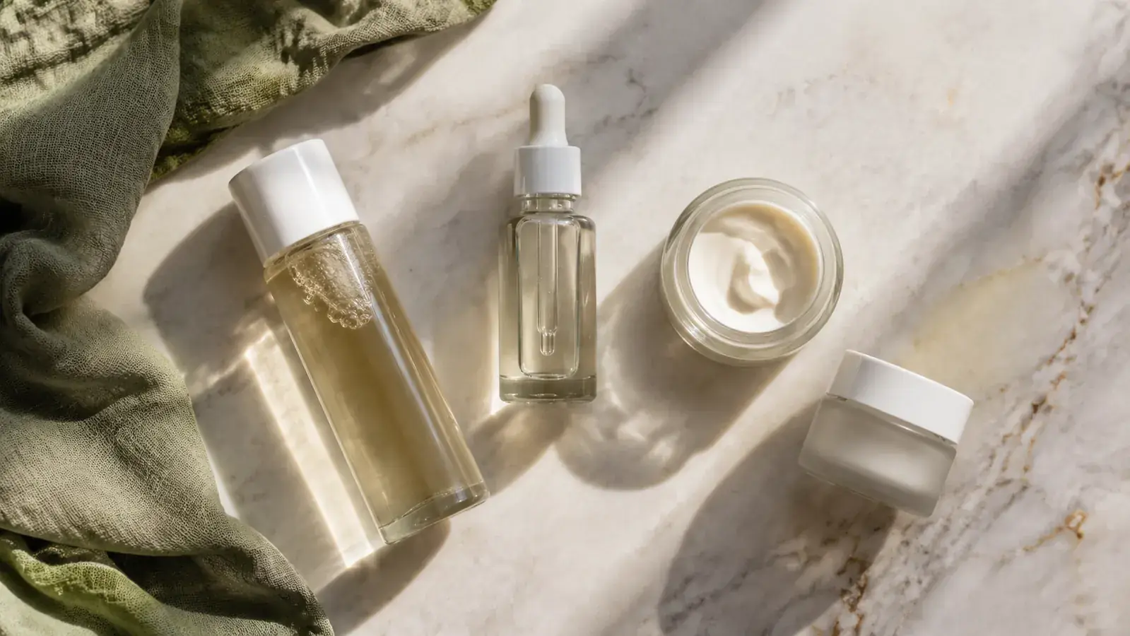 Skincare flatlay showing retinol serum, niacinamide, ceramide moisturizer, and SPF arranged on a marble surface