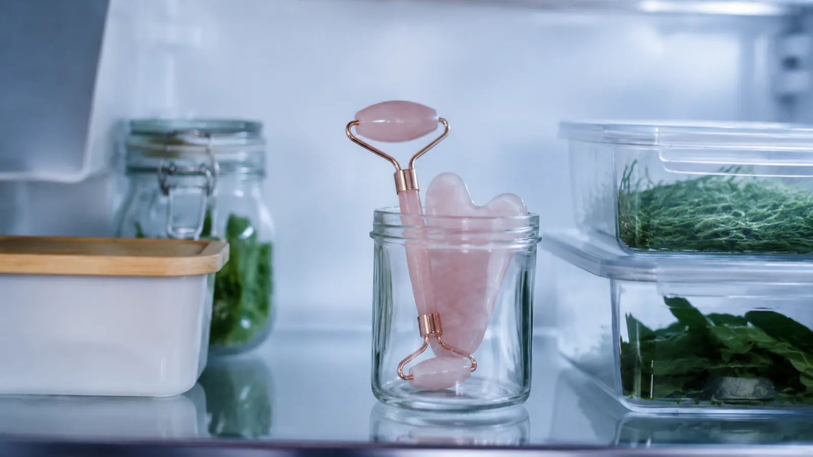 Rose quartz roller and gua sha stone stored in a small container inside a refrigerator door shelf