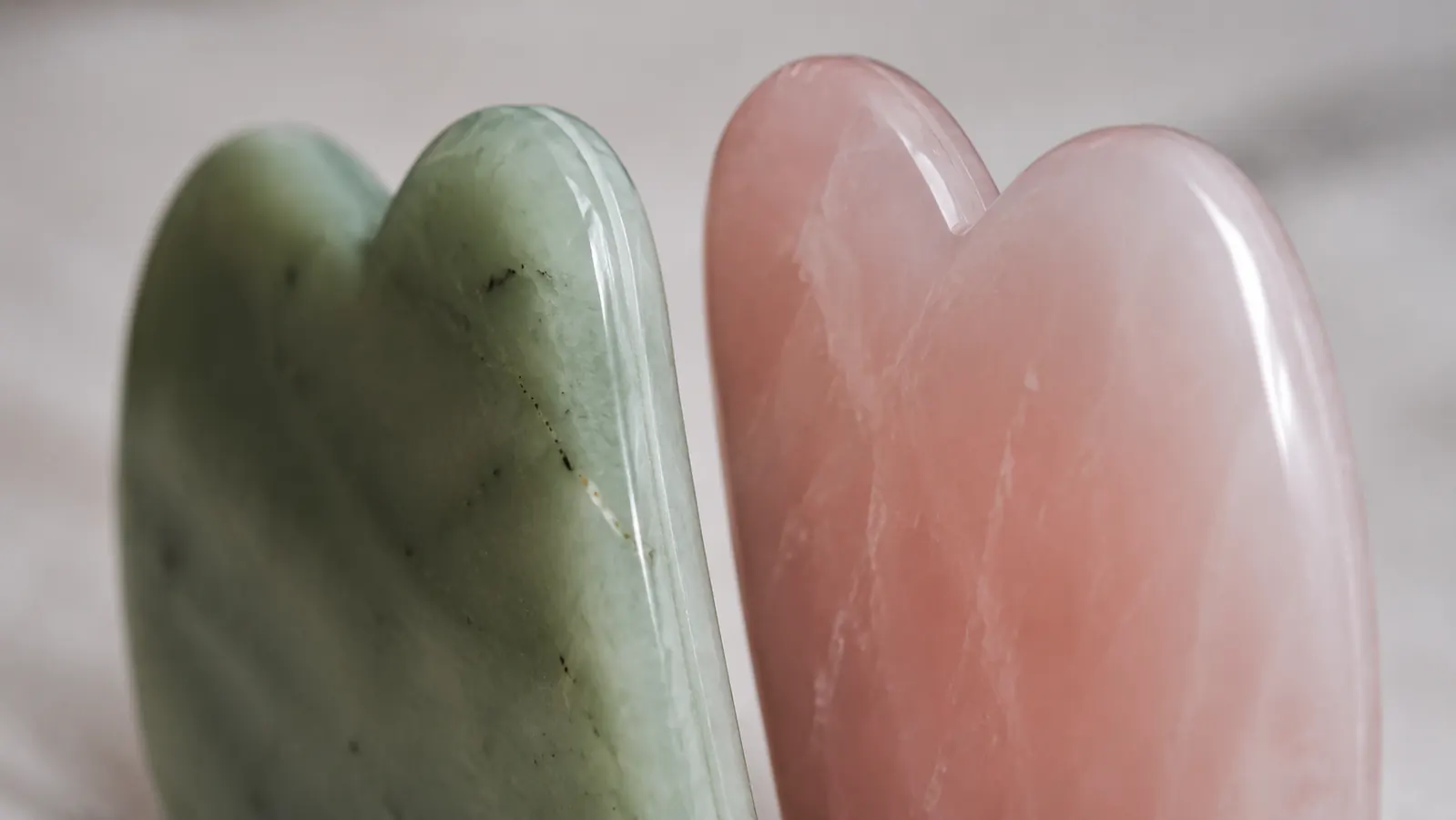 Close-up of a rose quartz gua sha stone showing visible mold seam line along the edge, next to a premium stone with clean beveled edges