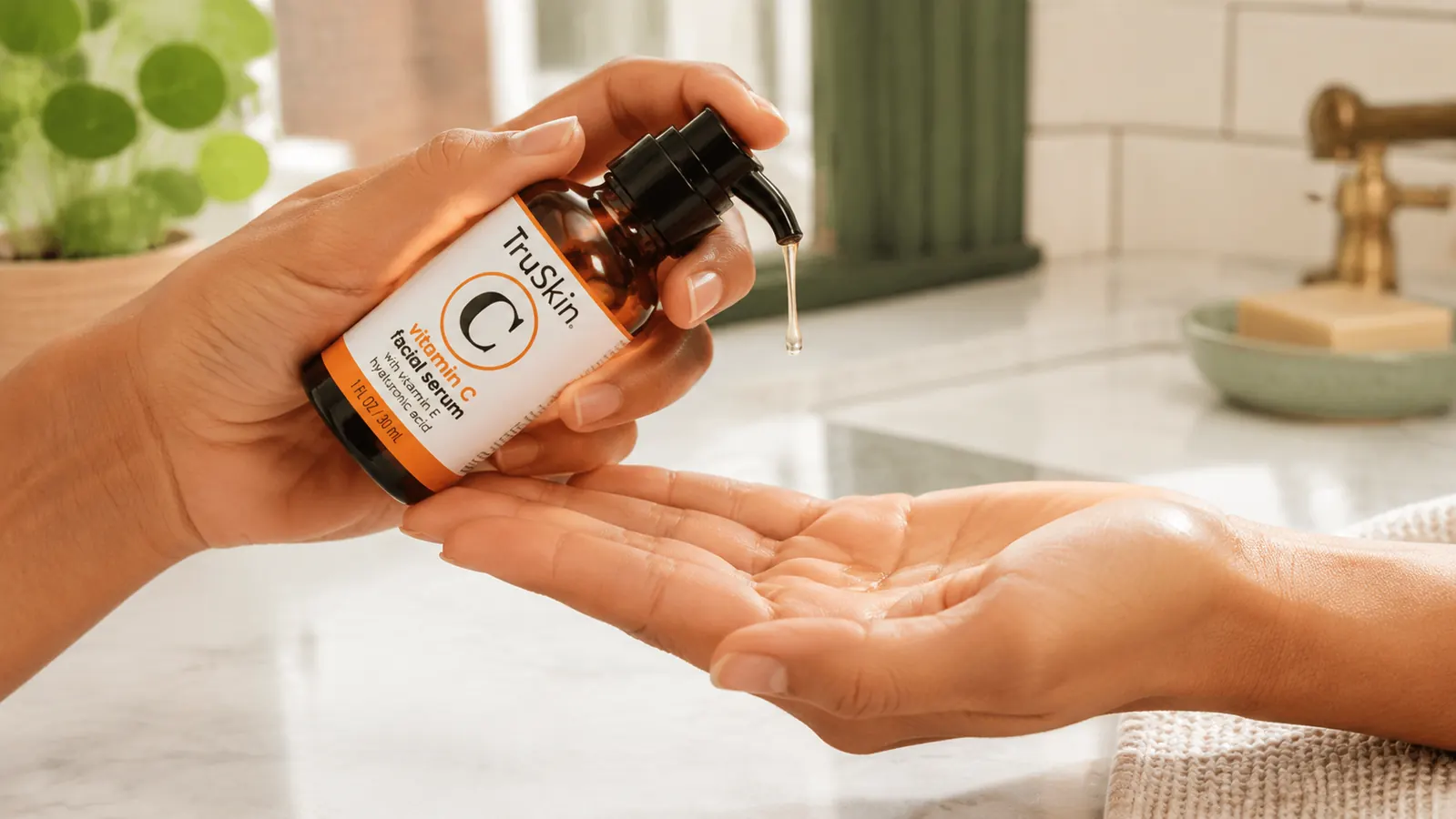Hand holding a small dark amber dropper bottle of TruSkin Vitamin C Serum over an open palm, bright neutral background